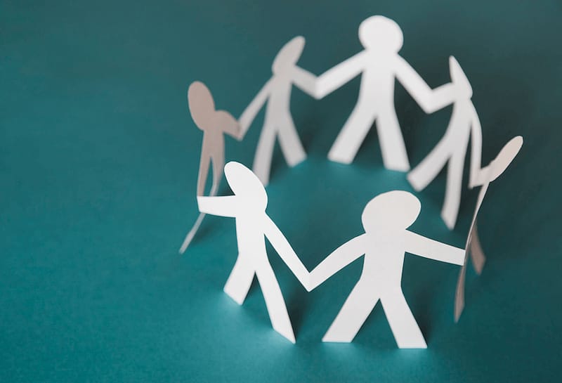 Collaboration Apps for Teams - Photo of white paper dolls holding hands in a circle on a blue-green background